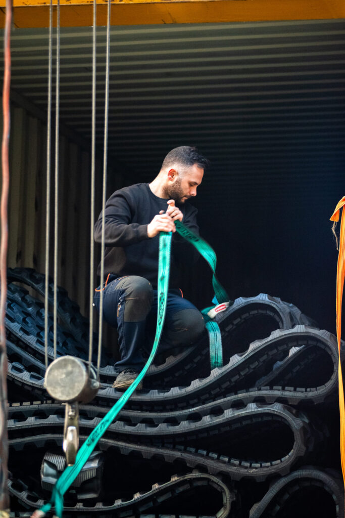 operario manipulando orugas de goma para maquinaria compacta en contenedor